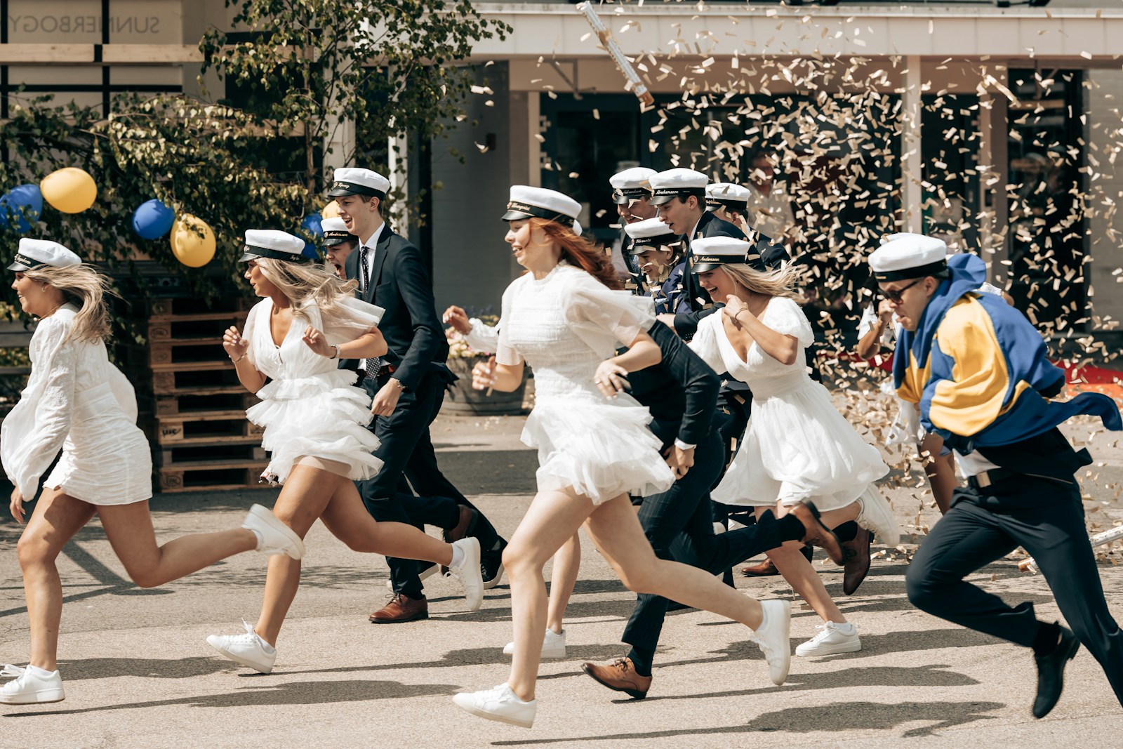 Graduates in white dresses run, celebrating their milestone.